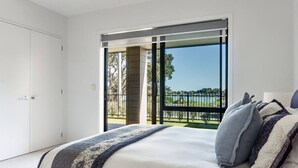 A bedroom with a large bed, a view of a park, and a sliding door leading to an outdoor area. - Okiwi Landing • Stylish • Central (Raglan)