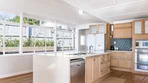 A modern kitchen with a central island, wooden cabinets, and a dishwasher. - Sunshine Rise • Magical Lorenzen Bay (Raglan)