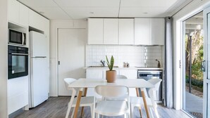 A modern kitchen with white cabinetry, a dining table with chairs, and a potted plant. - Sunshine Rise • Magical Lorenzen Bay (Raglan)