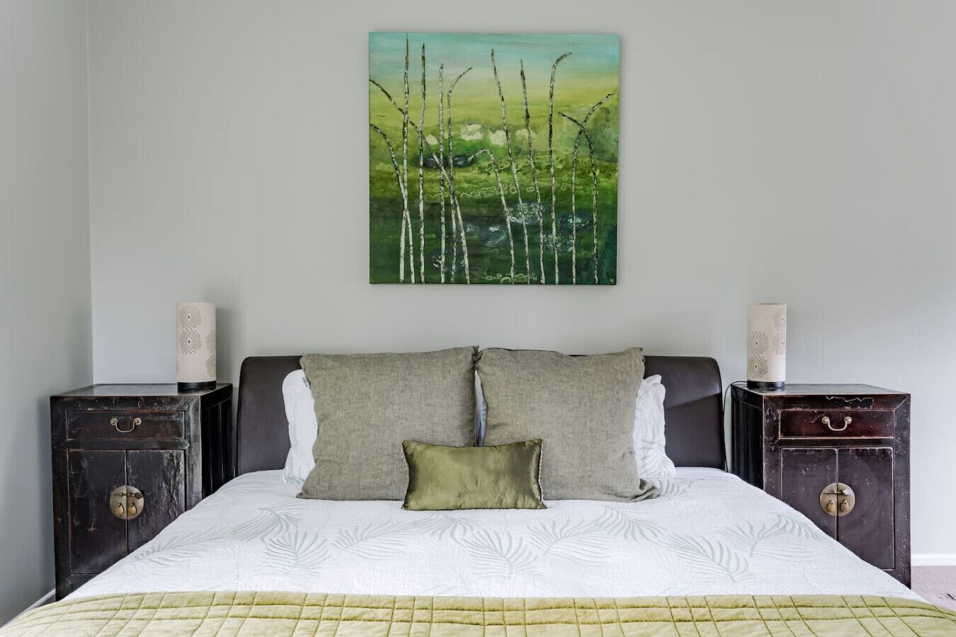 A bedroom with a bed, two nightstands, a painting, and a quilted bedspread.
