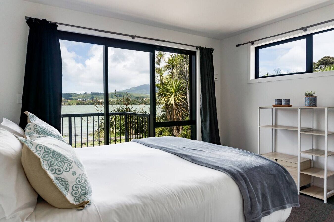 A bedroom with a large bed, a view of a body of water, and a balcony with a railing.