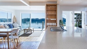 Eine moderne Küche mit einer großen Kochinsel, einem Essbereich mit Tisch und Stühlen und Seeblick durch große Fenster.