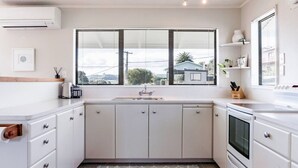 A modern kitchen with white cabinetry, a built-in oven, and a window with blinds. - Harbourside Cove • Views, Cosy + Peaceful (Raglan)