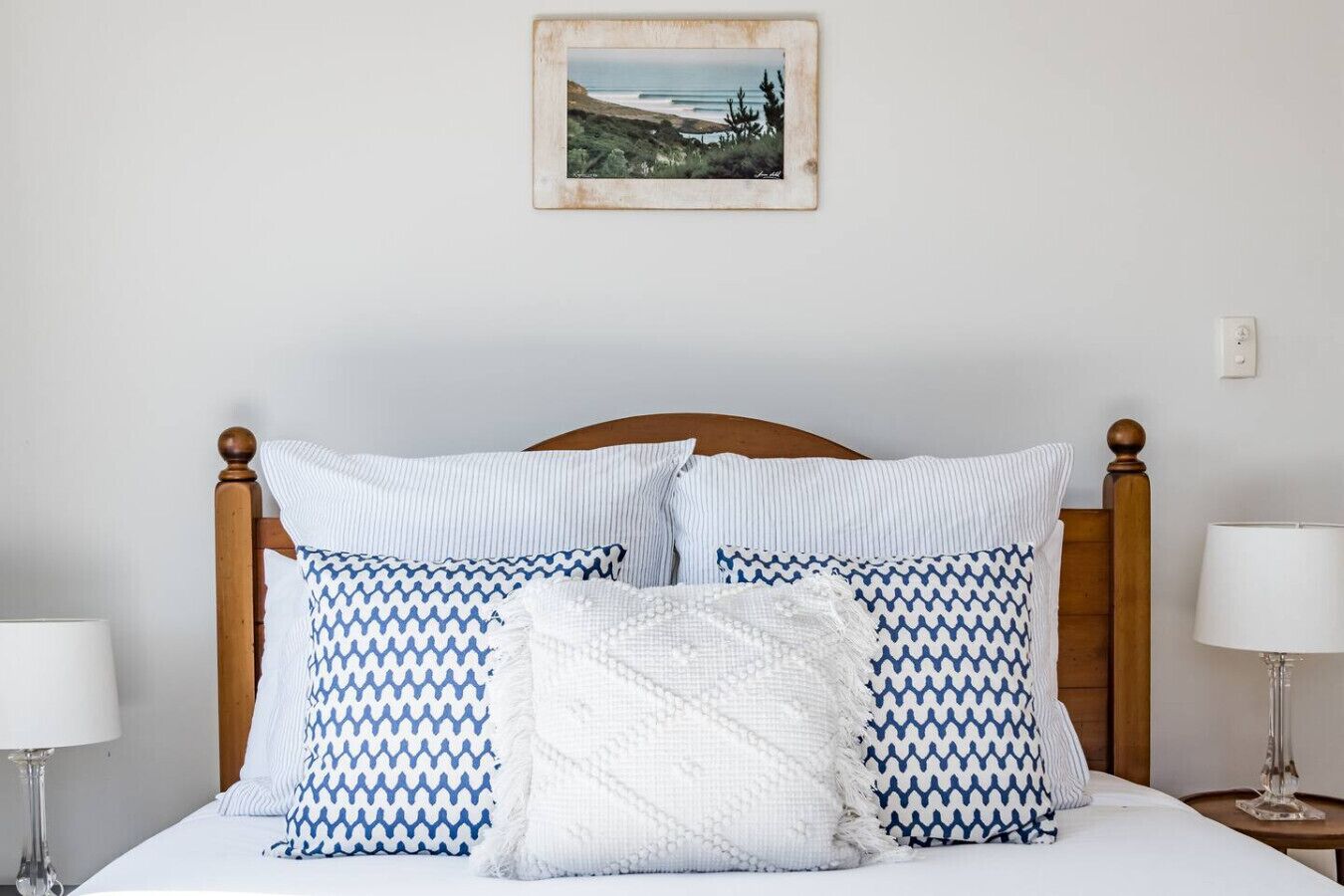 A neatly made bed with striped and patterned pillows, a framed picture on the wall, and bedside lamps.