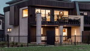 Ein modernes, zweistöckiges Haus mit Balkon, großen Fenstern und einem schwarzen Zaun.
