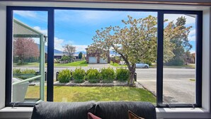 Une pièce dotée d’une grande fenêtre donnant sur une rue de banlieue, un petit jardin et offrant une vue sur une maison.