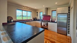 A modern kitchen with a large island, stainless steel appliances, and large windows offering views of the outdoors. - Fiordland Family Favourite (Te Anau)