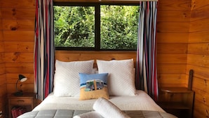 Un dormitorio de cabaña de madera con una cama, almohadas y una ventana con cortinas.