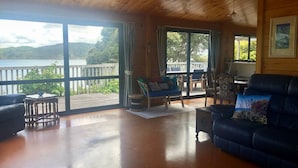 Amplia sala de estar con piso de madera, grandes puertas corredizas de vidrio que dan a una terraza y vista a un lago.