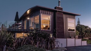 A modern house with large windows, a visible interior, and a well-maintained garden. - Government House • Spa • Comfort • Views (Raglan)