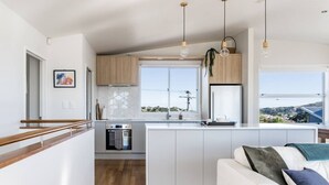 A modern kitchen with a central island, wooden cabinets, and pendant lighting. - Government House • Spa • Comfort • Views (Raglan)