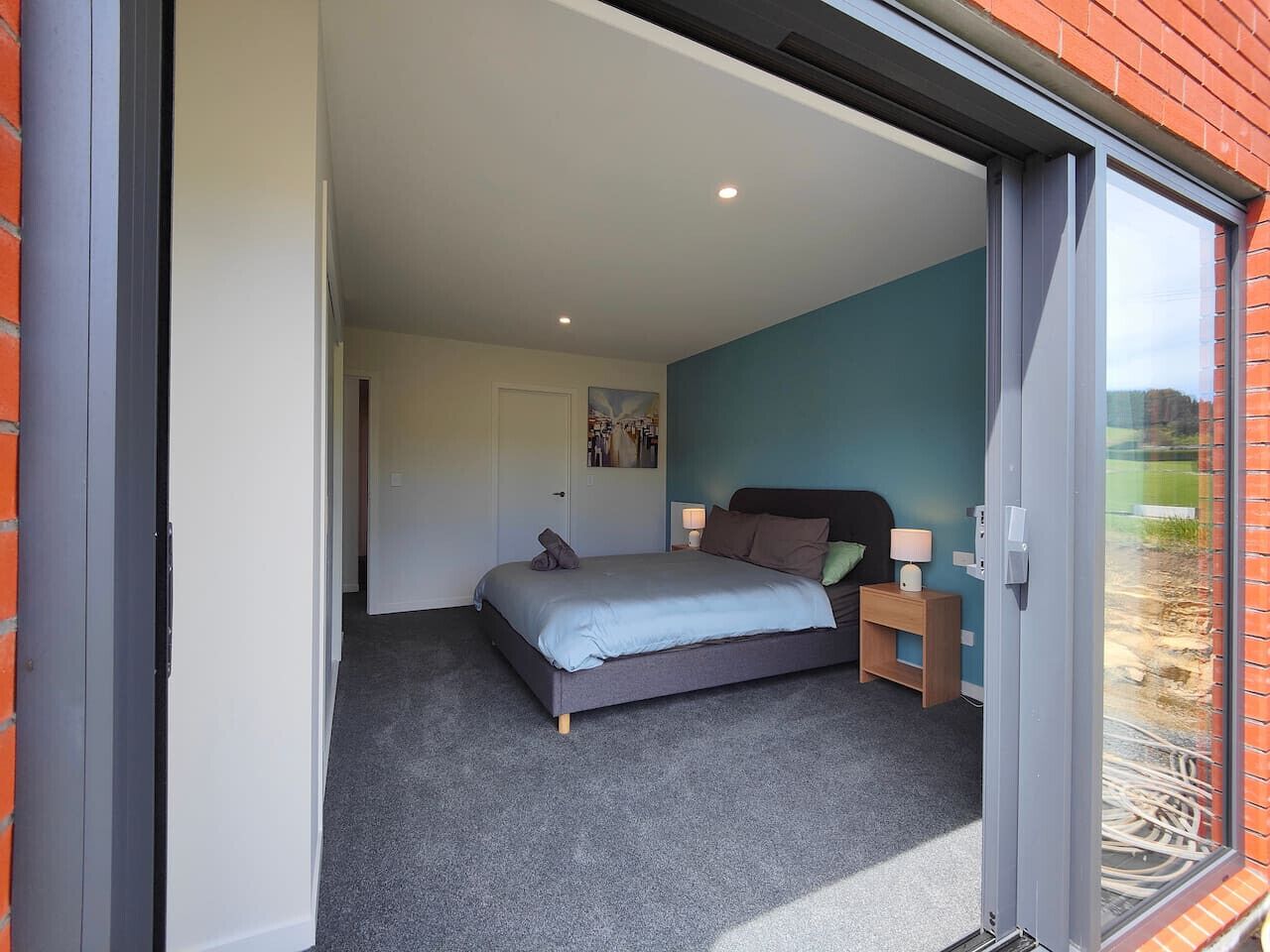 A bedroom with a bed, nightstands, and a sliding glass door leading to an outdoor area.