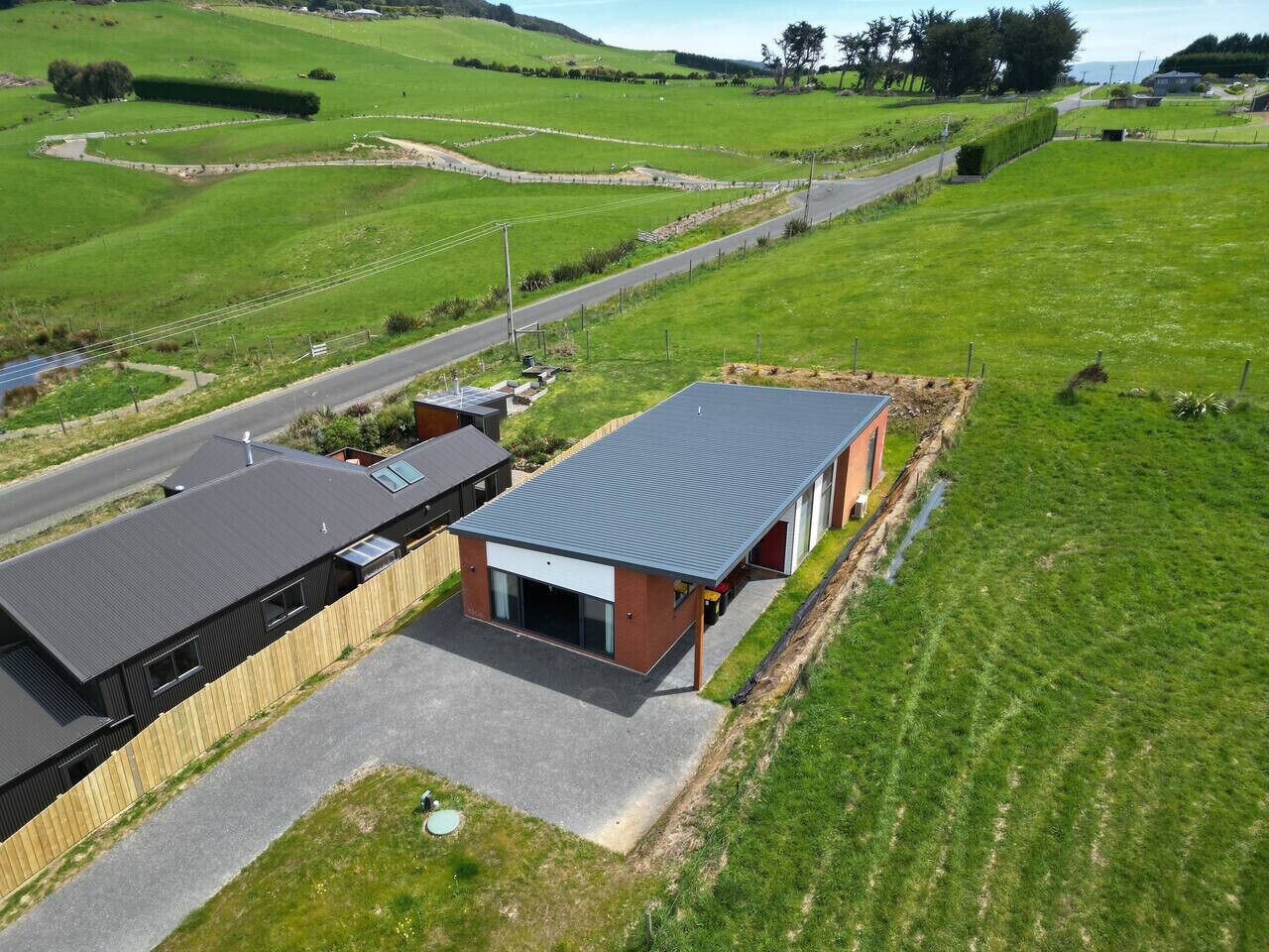 A modern building with a flat roof, adjacent to a road, surrounded by green fields.