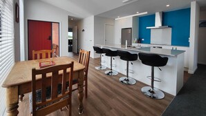 A modern kitchen with a central island, bar stools, and a dining table with chairs. - Rack n Relax Riverton (Riverton / Aparima)