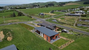 A modern building with a flat roof and a small attached garage, surrounded by green fields and a road. - Rack n Relax Riverton (Riverton / Aparima)
