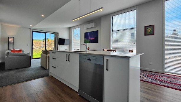 A modern kitchen with a dishwasher, a dining area with a sofa, and large windows. - Rack n Relax Riverton (Riverton / Aparima)
