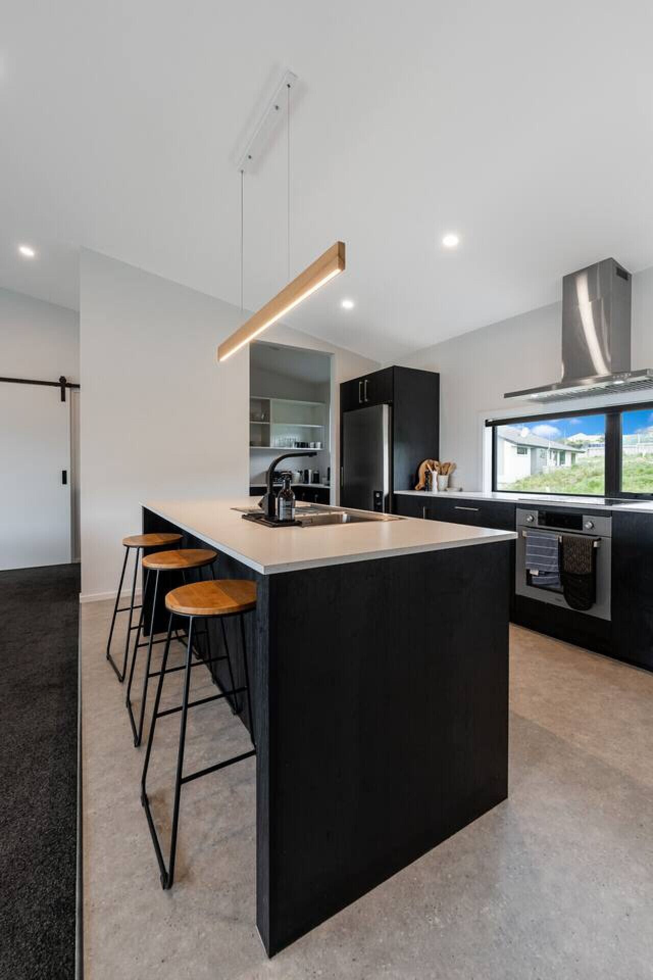 Una cocina moderna con una isla central, taburetes de bar, horno empotrado y vistas al exterior.