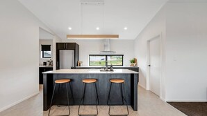 A modern kitchen with a central island, three bar stools, a large window, and a view of the outdoors.