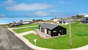 A modern house with a black exterior, a deck, and a view of the ocean.