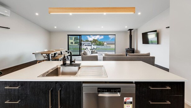 A modern kitchen with a dishwasher, a dining area with a table and chairs, a sofa, and a TV mounted on the wall.