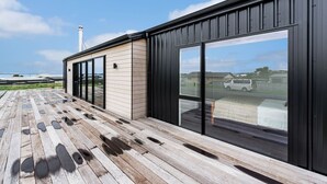 A modern building with large sliding glass doors, a wooden deck, and a view of a residential area.