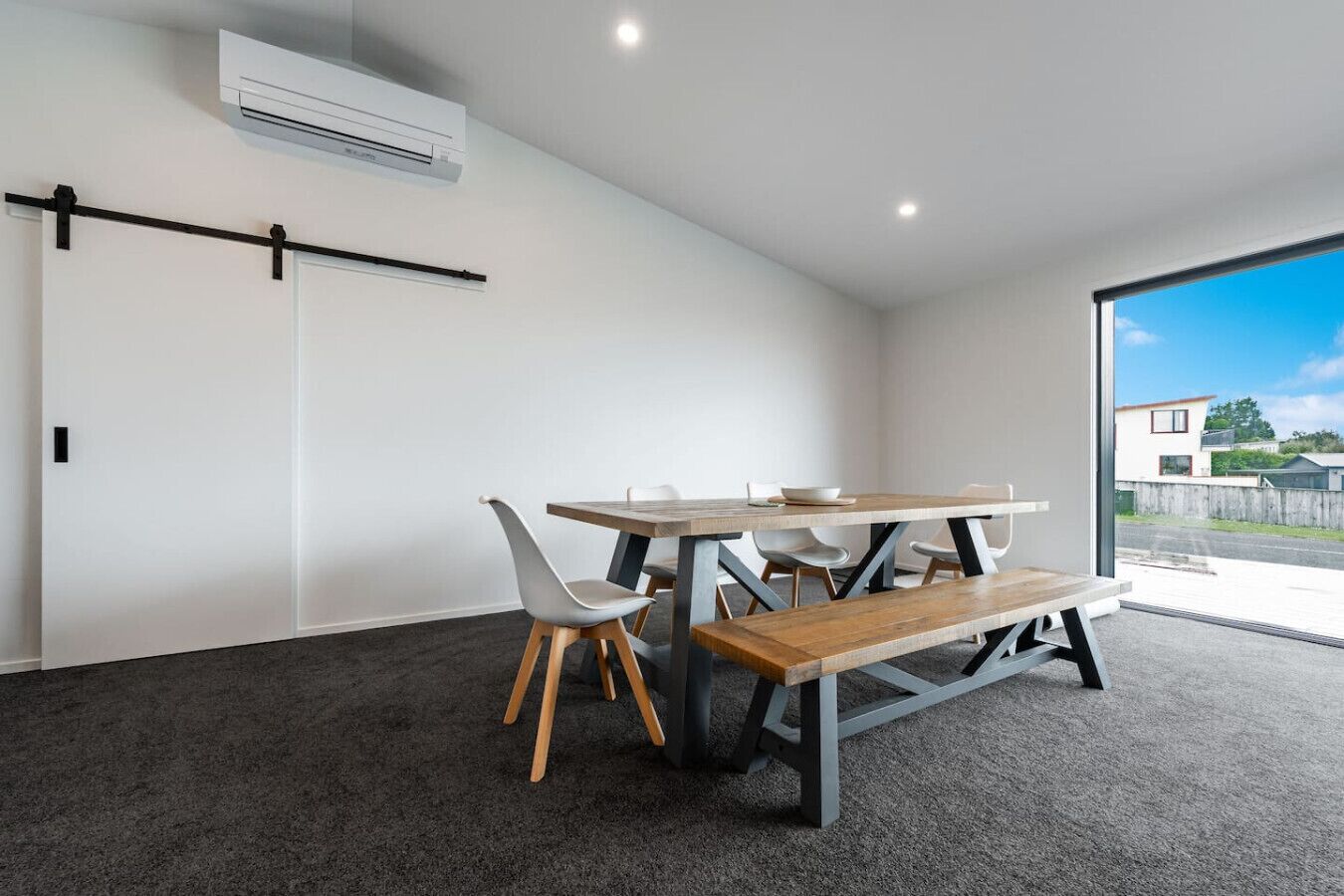 Een moderne eethoek met een houten tafel en banken, witte stoelen en een zwarte metalen bar.
