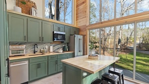 A modern kitchen with green cabinets, a marble countertop, and a large island. - Modern Black Cabin w/ Hot Tub (Burns)
