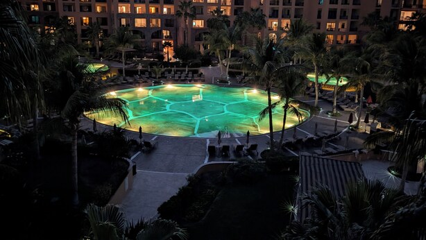 A resort with a swimming pool surrounded by palm trees and a mountain backdrop.