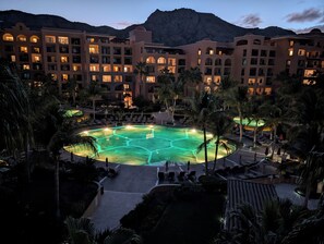 Un complexe hôtelier doté d’une piscine entourée de palmiers, avec une chaîne de montagnes en toile de fond.