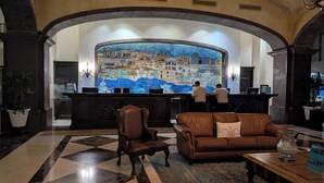 A lobby with a check-in counter, a brown leather sofa, a patterned rug, and a tiled floor.