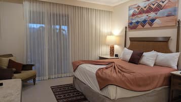 Une chambre d’hôtel avec un lit, une table de chevet, une lampe, une chaise et un tableau au mur.