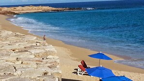 A beach with a stone wall, a few beach chairs, and blue umbrellas.