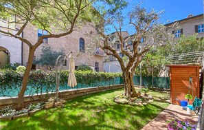 Un cortile con piscina, alberi e una piccola struttura in legno.