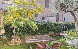 Un giardino con tavolo e sedie di legno, un siepe e un edificio sullo sfondo.