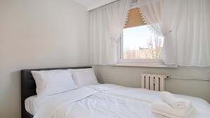 A neatly made bed with white linens, a dark headboard, and a window with white curtains. - Park Podolski Deluxe Apartment (Łódź)