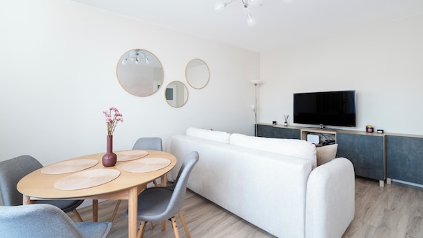 A modern living room with a dining area, a sofa, a TV, and a ceiling light fixture. - Park Podolski Deluxe Apartment (Łódź)