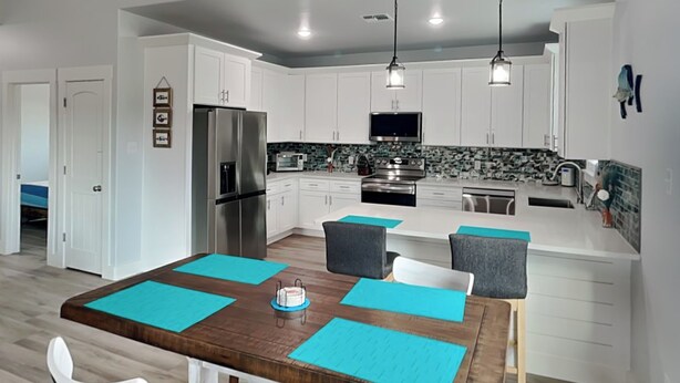 A modern kitchen with white cabinets, stainless steel appliances, and a central island with seating. - Coastin' (Rockport)