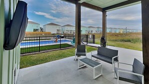 A covered patio with outdoor furniture, a pool, and a view of residential buildings. - Coastin' (Rockport)