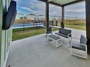 Eine überdachte Terrasse mit Gartenmöbeln, einem Pool und Blick auf Wohnhäuser.