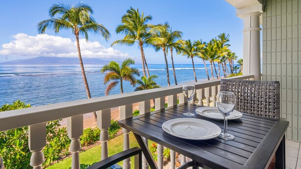 Ein Balkon mit Tisch für zwei Personen, mit Blick auf einen Strand mit Palmen und dem Meer.