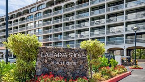 Ein mehrstöckiges Hotel mit Balkonen, einem Schild aus Stein mit der Aufschrift "LAHINA SHORES BEACH RESORT" und angelegten Gärten.