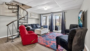 A modern living room with a staircase, a red chair, a black chair, a white sofa, and a painting on the wall.