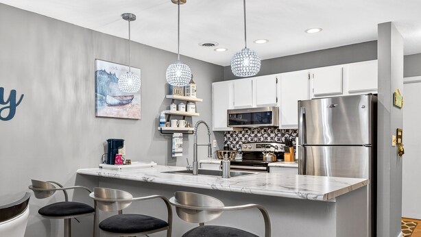 A modern kitchen with a marble countertop, stainless steel appliances, and bar stools.