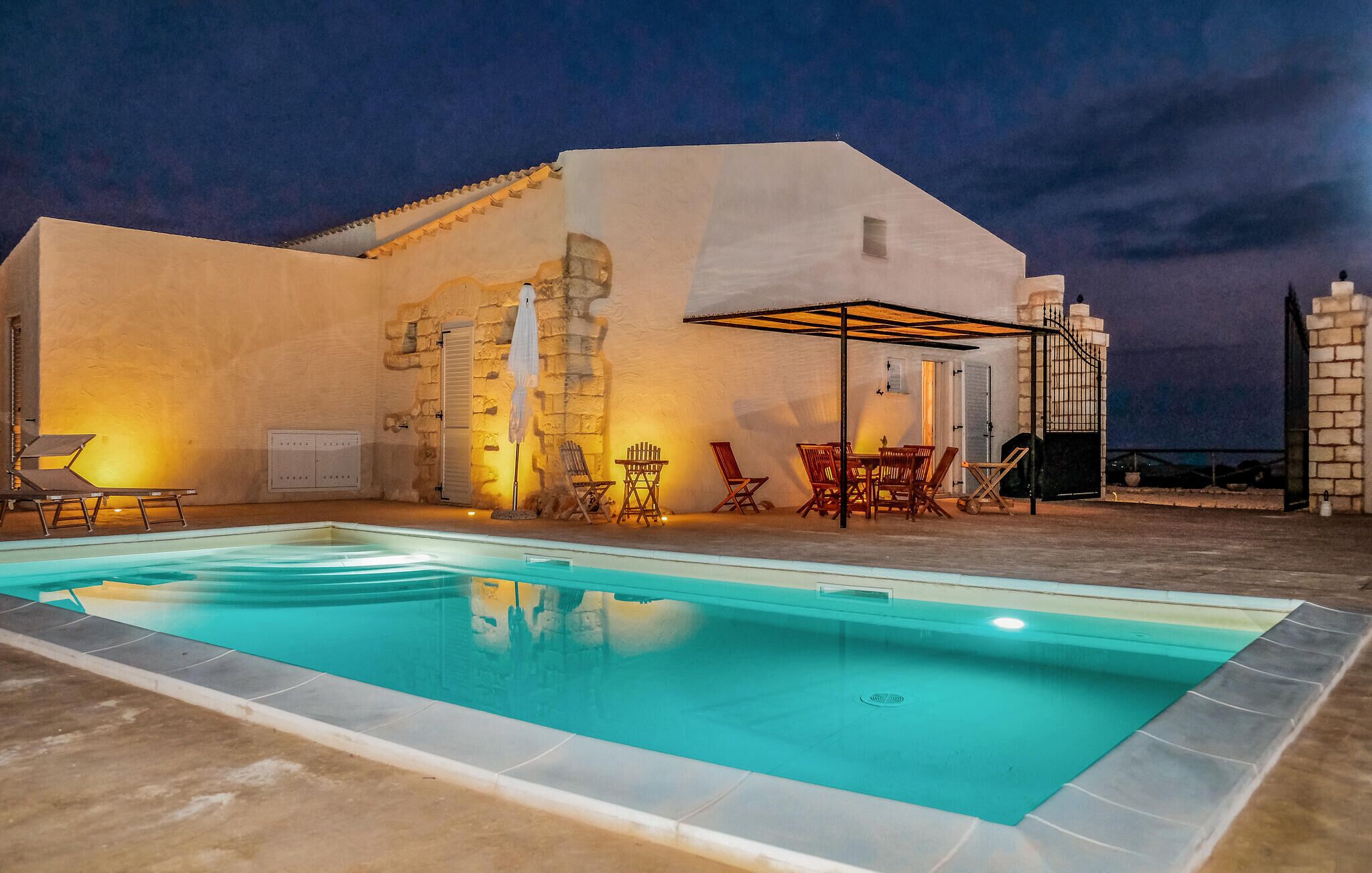 A swimming pool with a patio area, outdoor seating, and a stone wall.