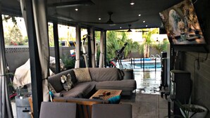 Ett takförsett utomhusområde med sittplatser, en soffa, stolar och en pool i bakgrunden.