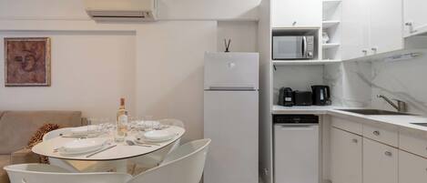 A modern kitchen with white cabinets, a refrigerator, a microwave, and a dishwasher. There is a dining table with chairs and a small decorative item on the refrigerator.