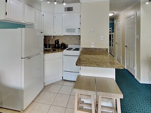 A compact kitchen with white cabinets, a stove, a microwave, and a sink. - Casa Del Mar 124 (Galveston)