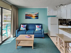 A living room with a blue sofa, a coffee table, and a painting on the wall. - Casa Del Mar 124 (Galveston)