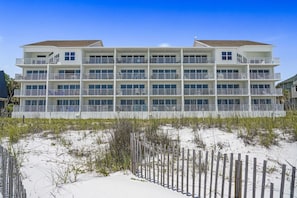 A multi-story hotel with balconies, located on a sandy beach with a wooden fence in the foreground. - Corner Unit Beachfront with Secluded Beach! (Destin)