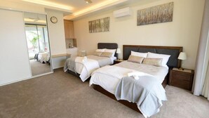 A modern hotel room with two beds, a large mirror, a ceiling fan, and artwork on the walls.